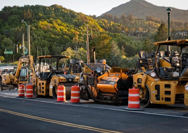 Road construction site with machinery and traffic cones under a scenic hill at sunset.
